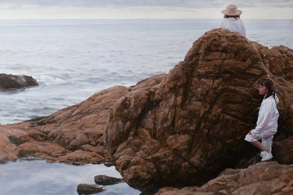 Two young girls wearing white outfits playing on big brown rocks on a beach