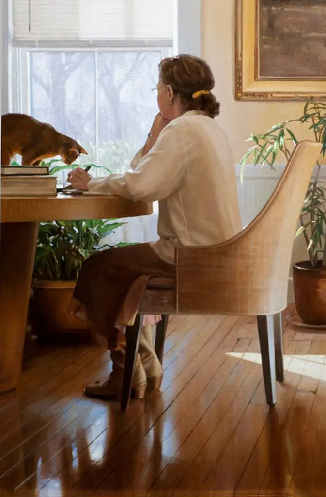 Woman sitting in a naturally lit office, looking out the window, with a cat sitting on the table looking at her hand holding a pen over paper