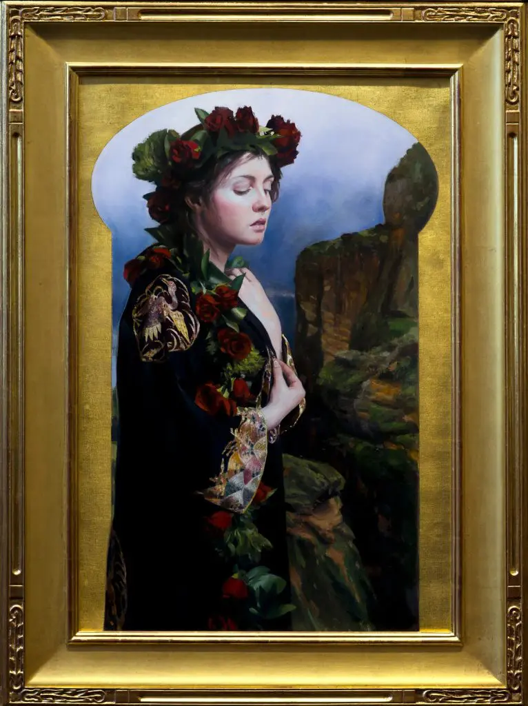 Woman wearing an ornate black gown with gold details and red rose garland in her hair, standing along a mountain side