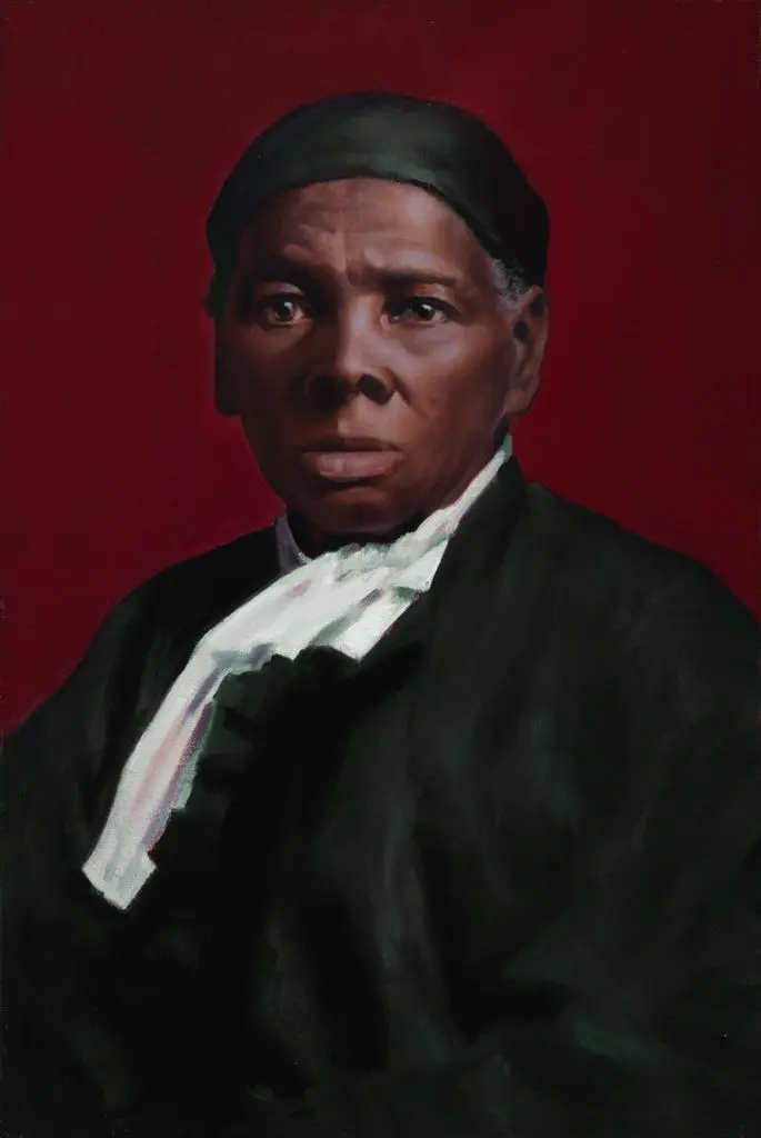 Bust of Harriett Tubman in her younger age, wearing a black cap and top, in front of a dark maroon backdrop