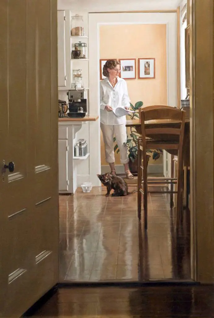 View of woman through a doorway, wearing white blouse and tan pants standing in a naturally lit office, with a cat sitting in front of her