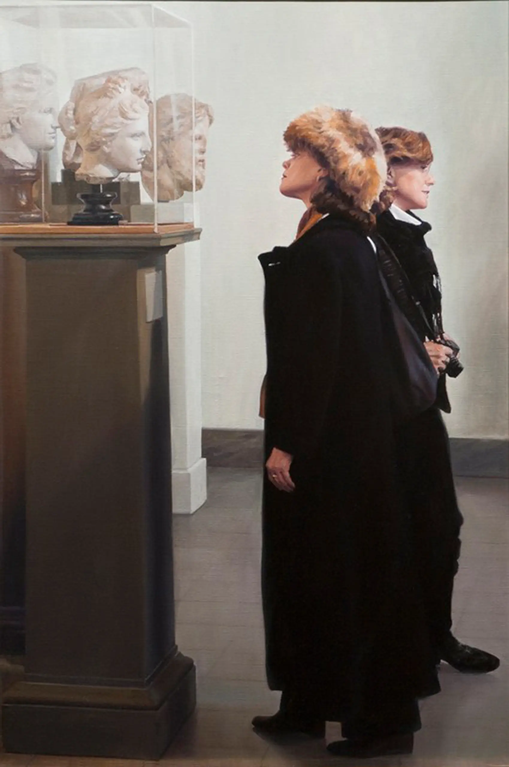 Young woman wearing a fur hat and black coat looking at a bust of a sculpture at a museum