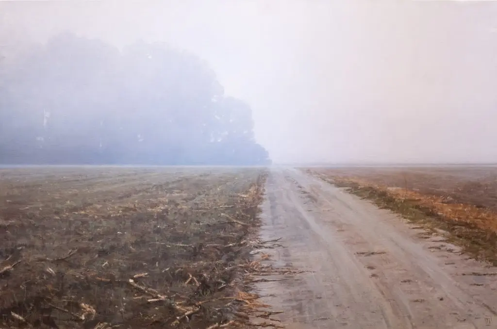 Foggy landscape of a dirt road and brown grass with trees off in the distance