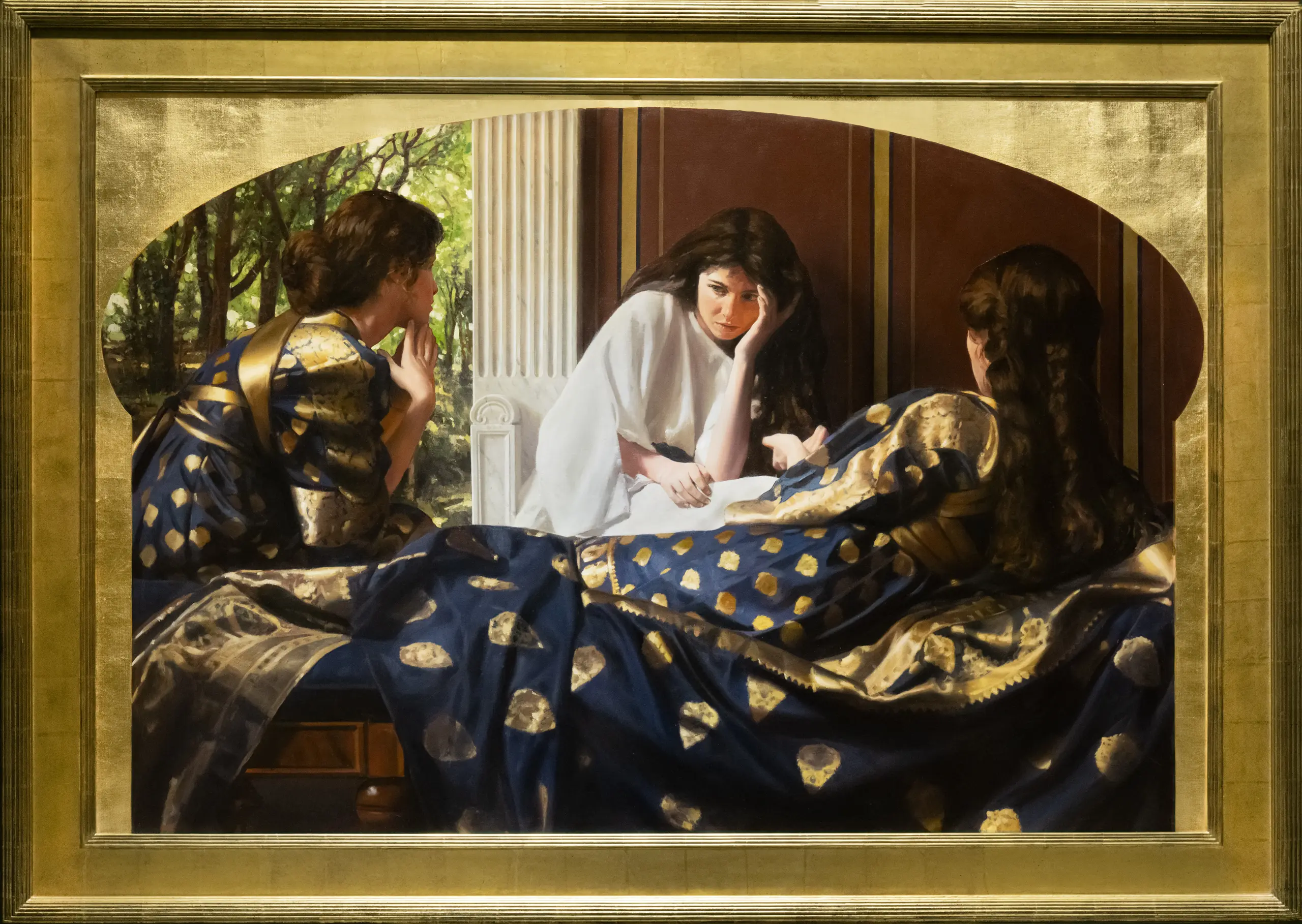 Three brunette women sitting together, two of them are wearing navy and gold robes and are facing a woman in a white robe with her face in her hand