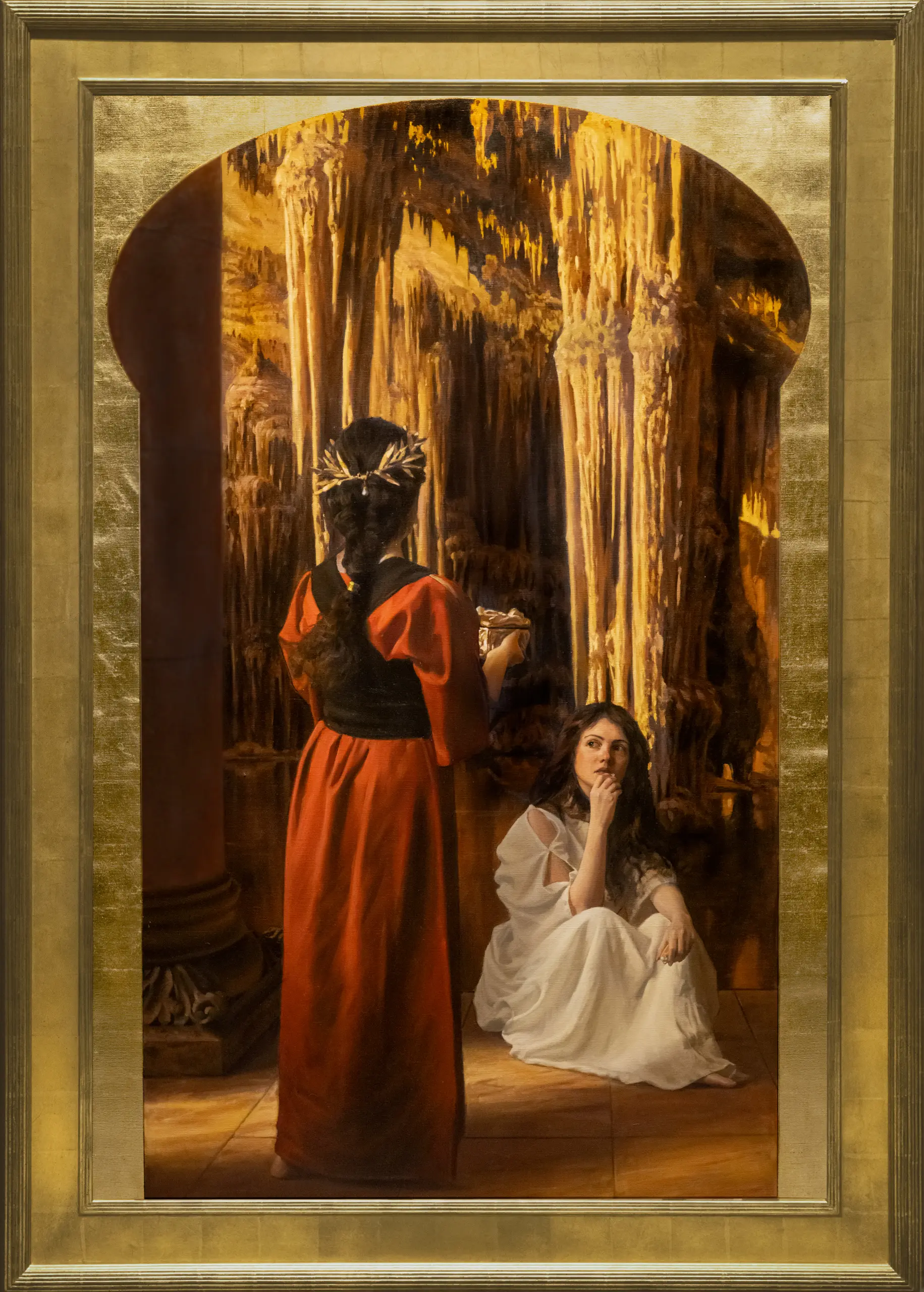 Woman with braided brown hair wearing a red robe, holding a basket and facing towards another brunette woman who is sitting on the floor in a gold colored room