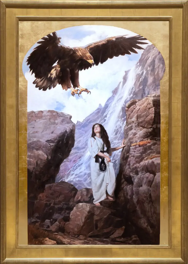 Large brown hawk flying down towards a woman wearing white robes standing on a cliffside