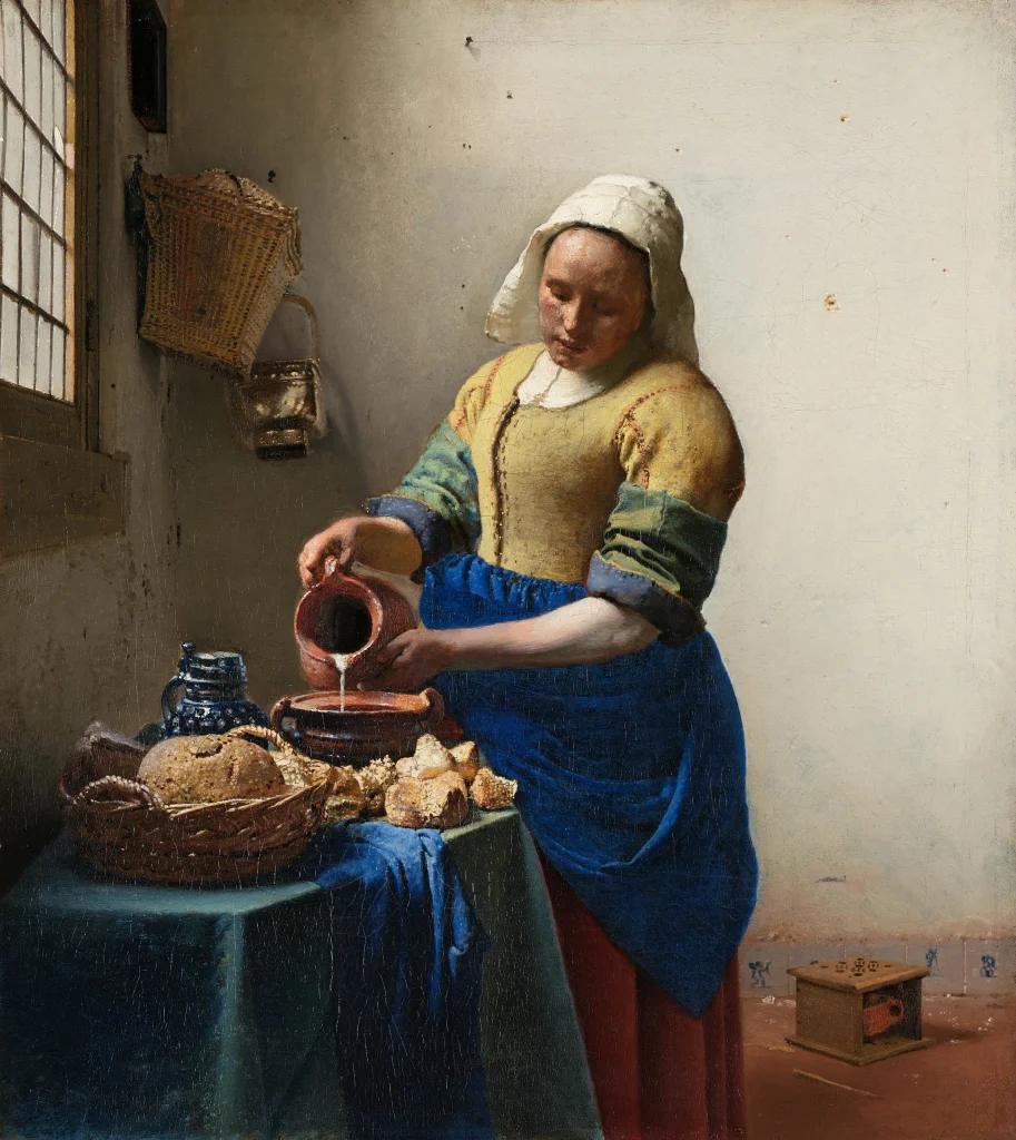 Woman wearing yellow top and blue apron, pouring milk into a bowl